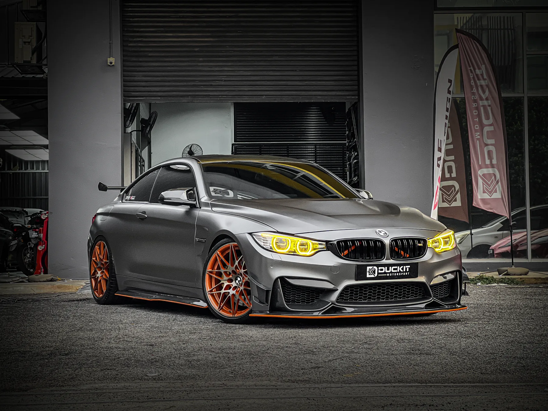Grey BMW M4 with widebody aero and yellow DRLs outside the Duckit workshop