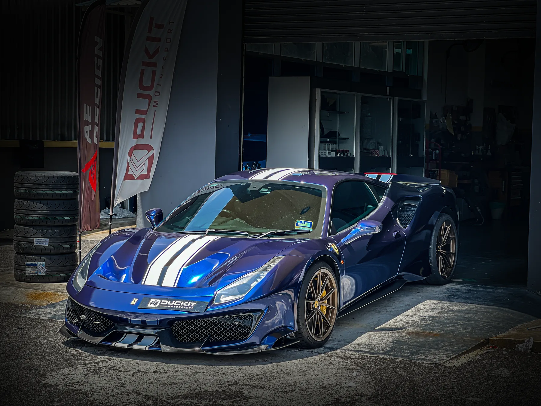 Blue Ferrari with white racing stripe parked outside the workshop